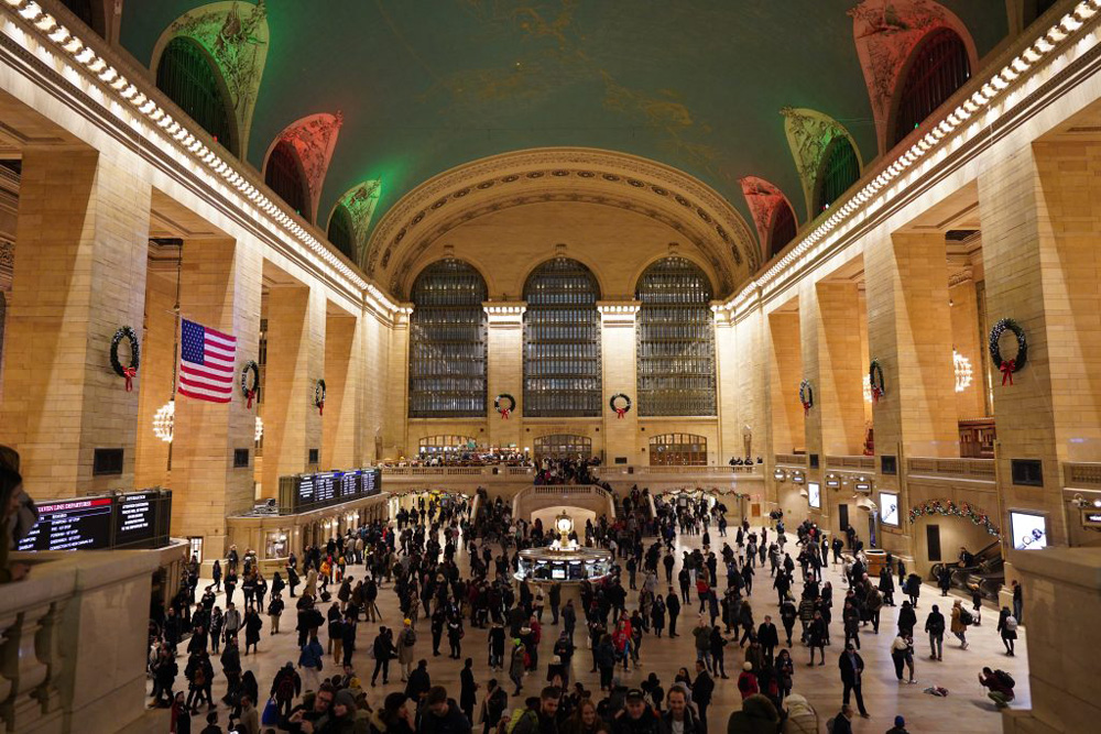 The image shows the grand central station in New York City. One of the most iconic train stations. Lit up on the inside with bright warm yellow lighting.