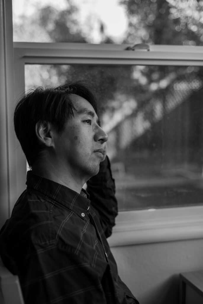 A black and white photo of a man from the side looking out the window.