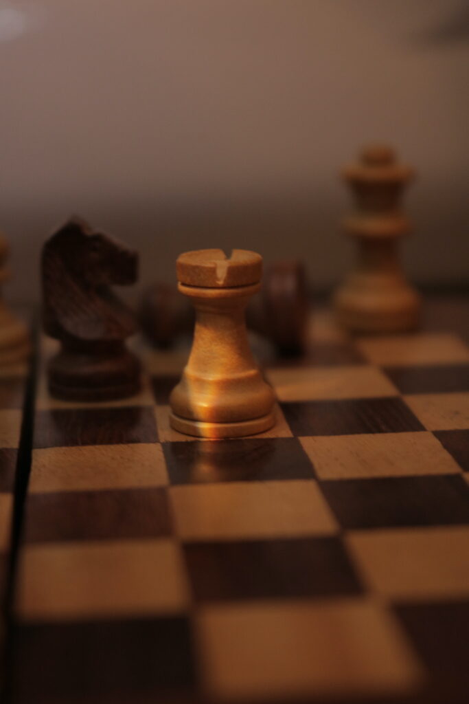 The squares on the chess board lead up to 4 chess pieces. 
The pieces in the background are out of focus with the rook in the middle of the image focused. There is a sliver of light on the rook